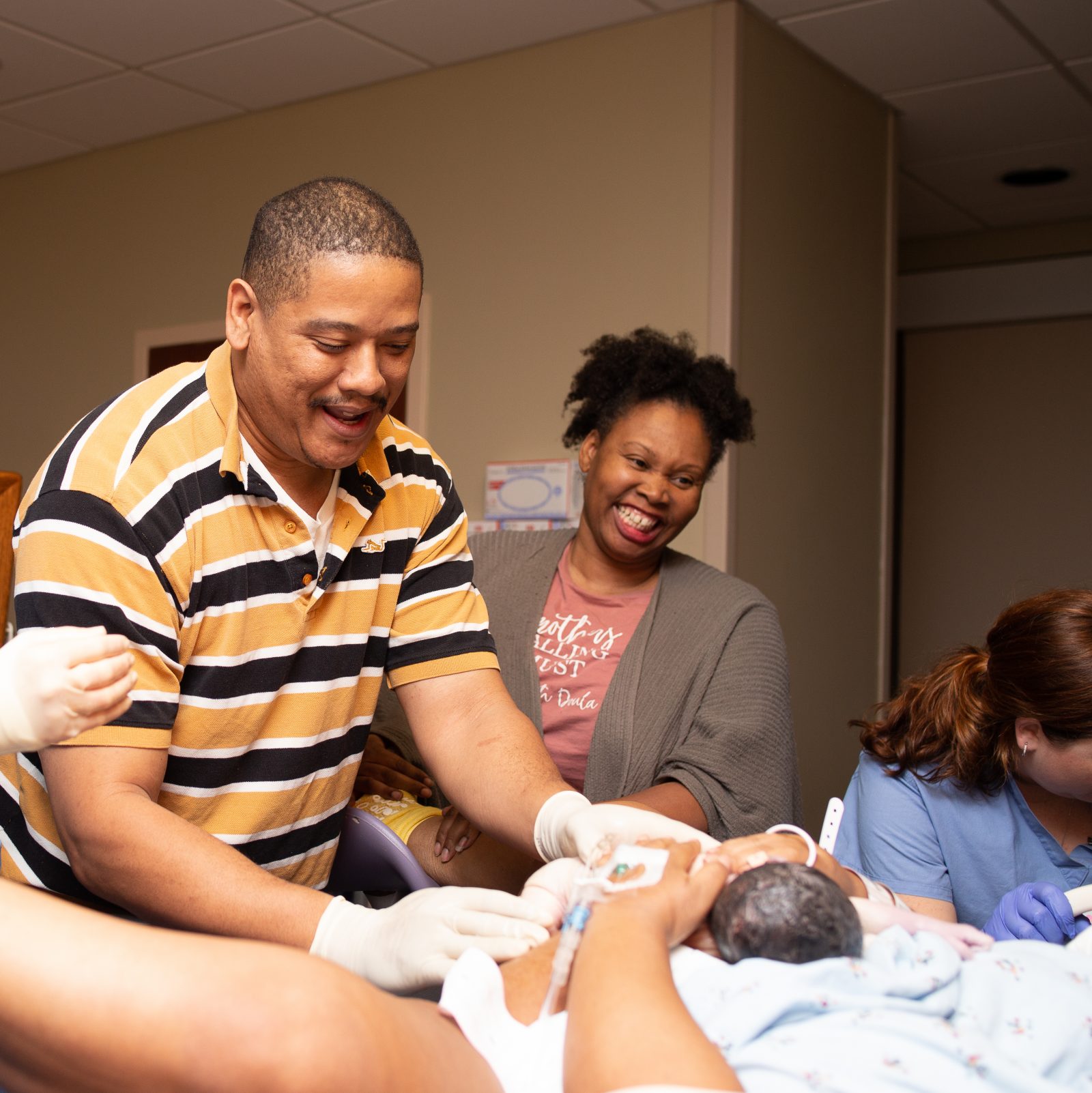 doula smiles as father helps deliver his baby