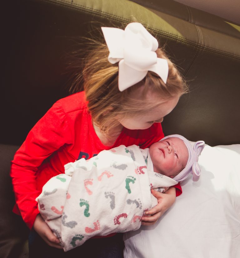 little girl holds swaddled newborn