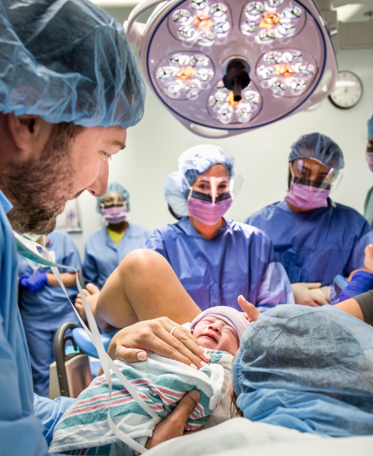 Father holds newborn for mother to ses while Doctor looks on